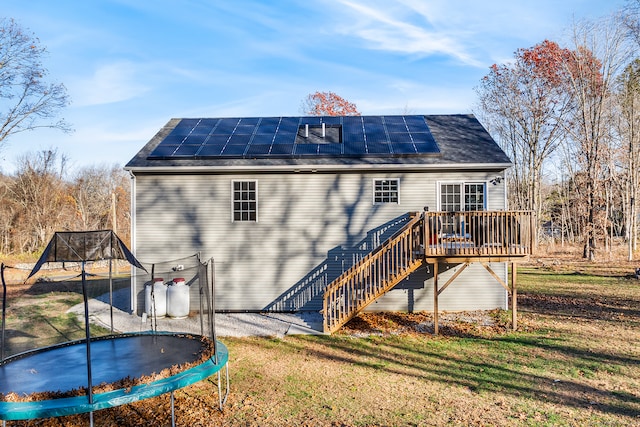 back of property with a lawn, solar panels, a deck, and a trampoline