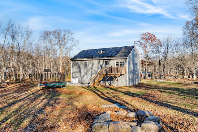 back of house featuring solar panels, a wooden deck, a lawn, and a trampoline