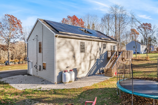 back of house with a trampoline, a yard, and a wooden deck