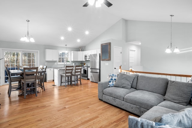 living room with ceiling fan with notable chandelier, light hardwood / wood-style floors, and high vaulted ceiling