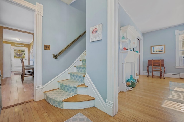 staircase featuring hardwood / wood-style flooring, crown molding, and a baseboard heating unit