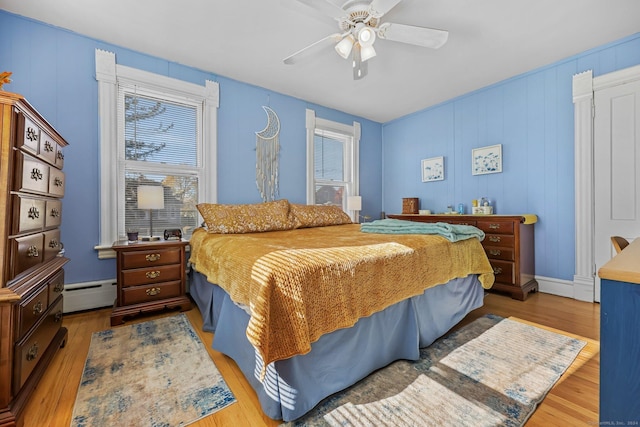 bedroom with light wood-type flooring, ceiling fan, and a baseboard heating unit