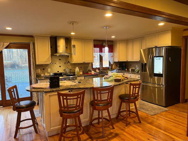 kitchen featuring appliances with stainless steel finishes, light wood-type flooring, dark stone counters, wall chimney exhaust hood, and pendant lighting