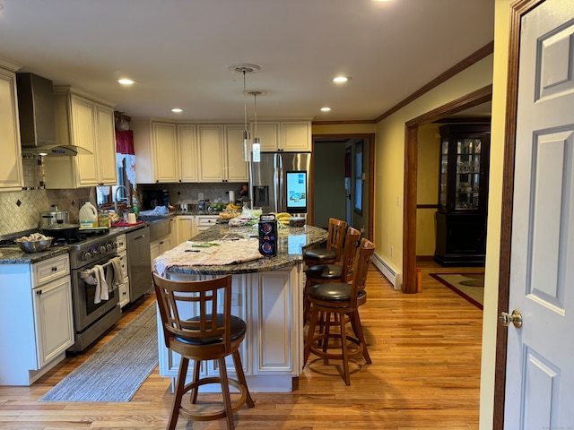 kitchen with wall chimney exhaust hood, stainless steel appliances, light hardwood / wood-style floors, a kitchen island, and hanging light fixtures