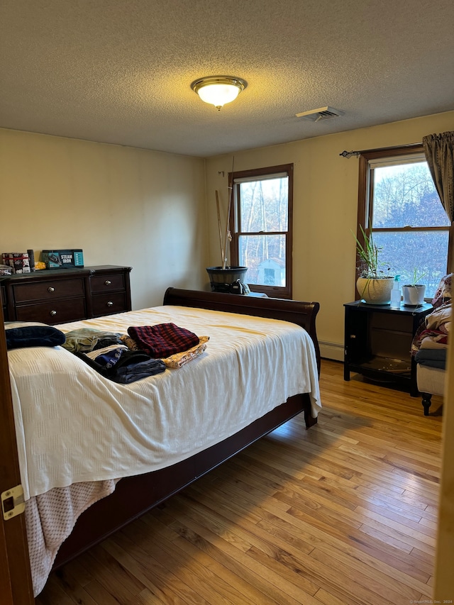 bedroom featuring light wood-type flooring, a textured ceiling, and multiple windows