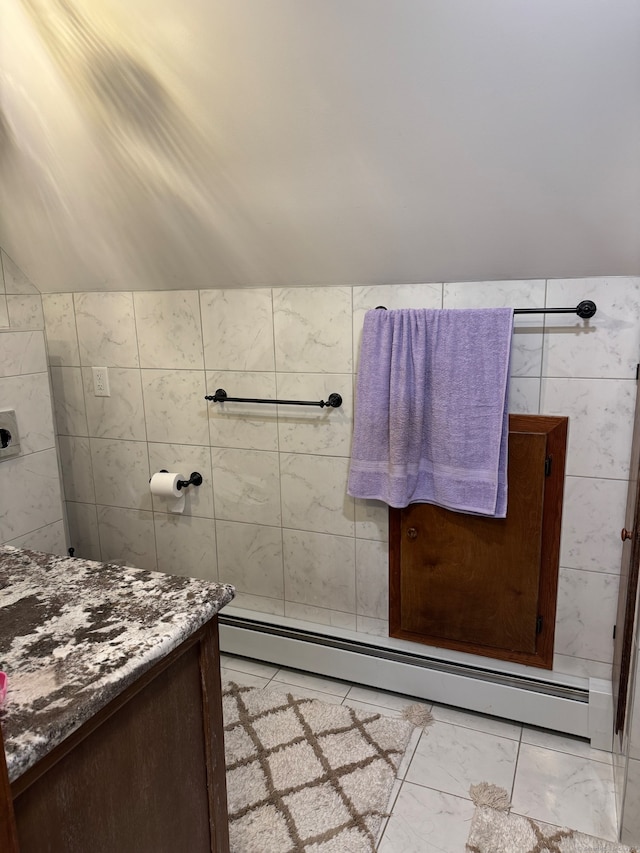 bathroom with vanity, vaulted ceiling, tile walls, and a baseboard heating unit