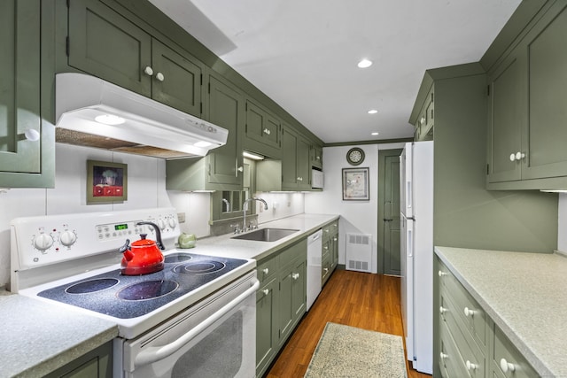 kitchen with white appliances, sink, green cabinetry, radiator heating unit, and dark hardwood / wood-style floors