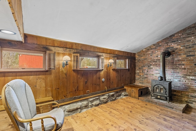 living area with wood walls, wood-type flooring, a wood stove, and vaulted ceiling