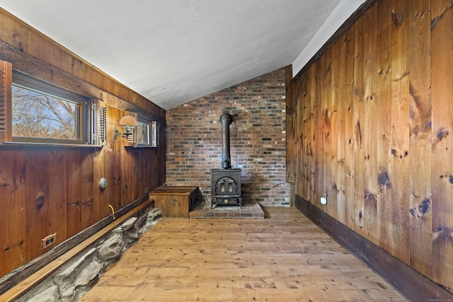 unfurnished living room featuring a wood stove, wooden walls, light hardwood / wood-style flooring, and vaulted ceiling