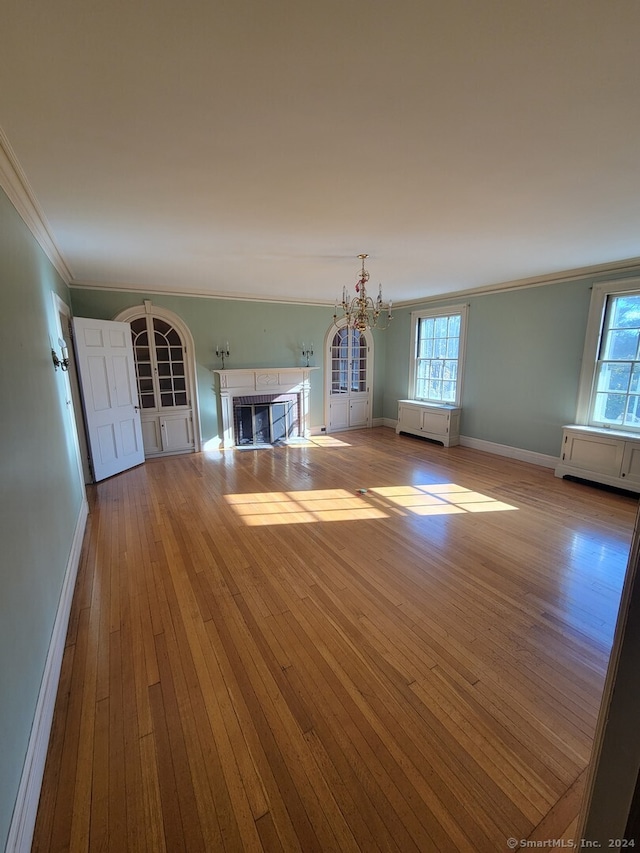 unfurnished living room featuring a chandelier, light hardwood / wood-style flooring, and crown molding