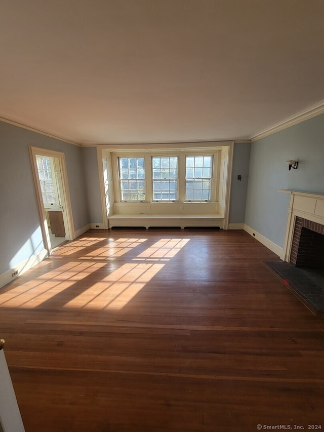 unfurnished living room with wood-type flooring, crown molding, and a brick fireplace