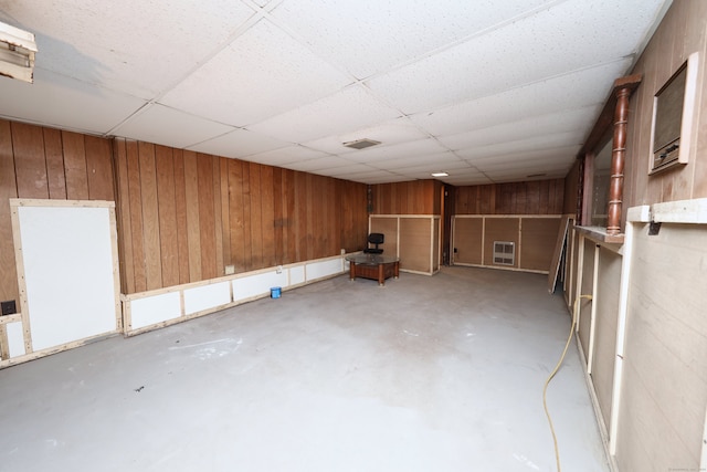 basement with a paneled ceiling, heating unit, and wood walls