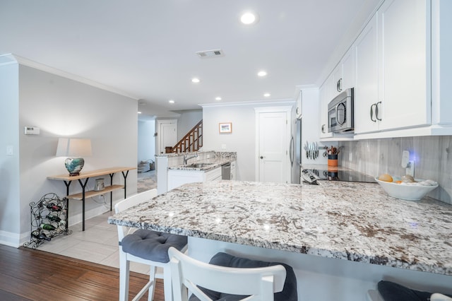 kitchen with kitchen peninsula, white cabinets, light stone countertops, and stainless steel appliances