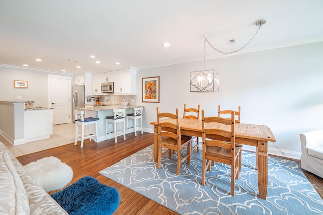 dining area with crown molding, an inviting chandelier, and light hardwood / wood-style flooring