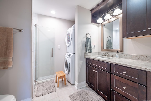 bathroom featuring toilet, a shower with shower door, stacked washer and clothes dryer, and vanity