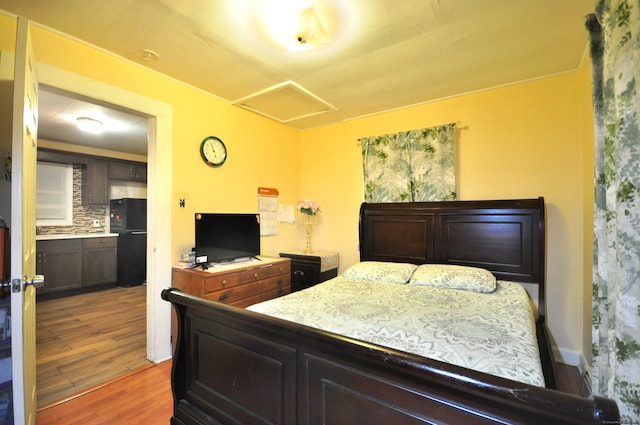 bedroom with black fridge and wood-type flooring