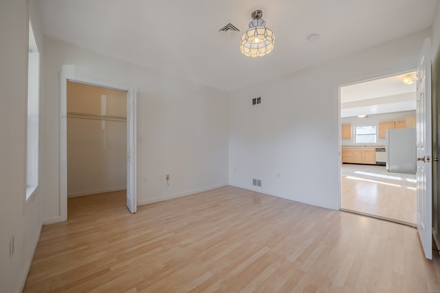 unfurnished bedroom featuring light hardwood / wood-style flooring, a spacious closet, a closet, and stainless steel refrigerator