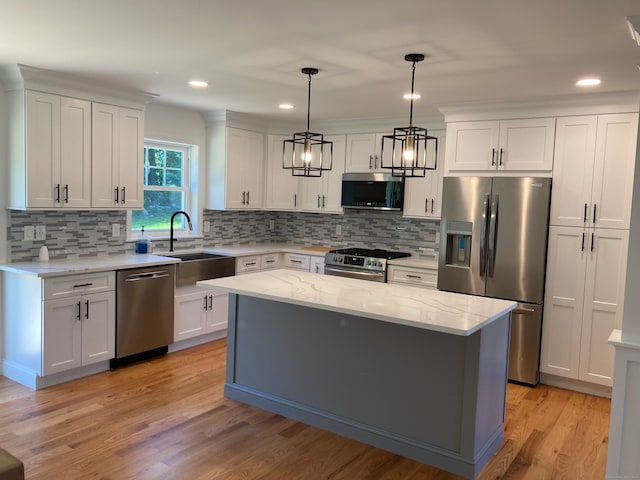 kitchen with white cabinetry, sink, stainless steel appliances, pendant lighting, and a kitchen island