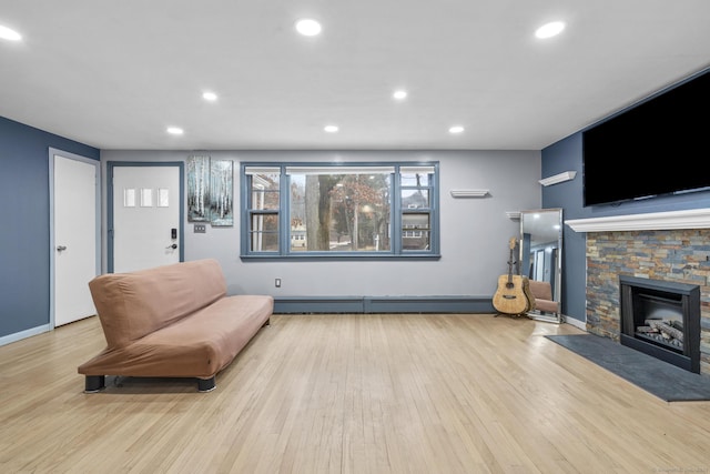 living area featuring a stone fireplace, a baseboard heating unit, and light wood-type flooring