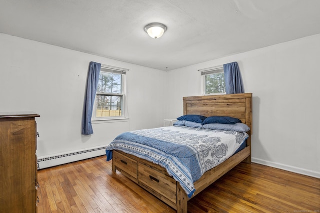 bedroom featuring hardwood / wood-style flooring, baseboard heating, and multiple windows