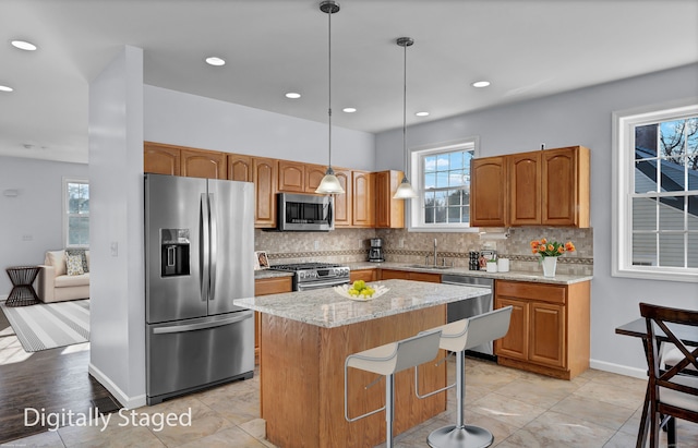 kitchen featuring light stone countertops, sink, a center island, pendant lighting, and appliances with stainless steel finishes