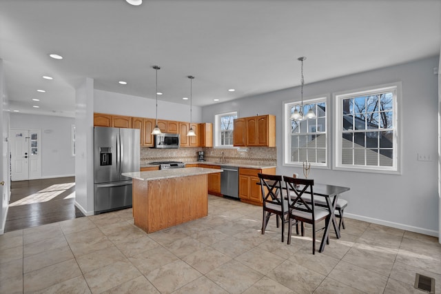 kitchen with tasteful backsplash, stainless steel appliances, light tile patterned floors, decorative light fixtures, and a center island