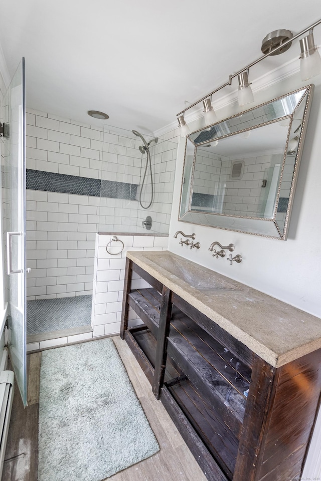 bathroom featuring a tile shower, a baseboard heating unit, crown molding, vanity, and hardwood / wood-style flooring