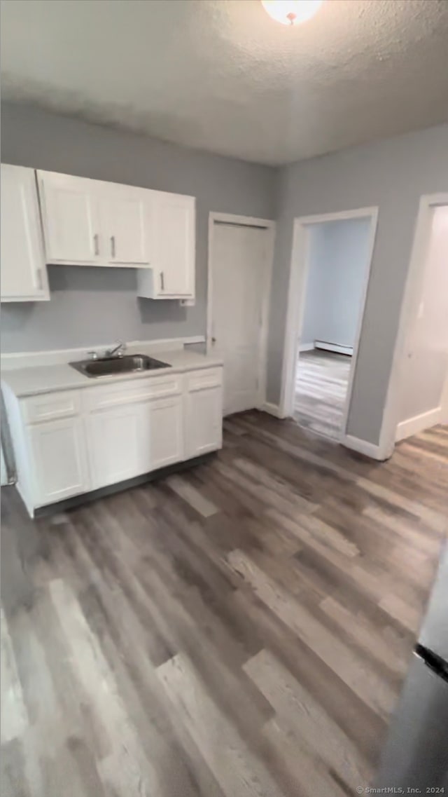 kitchen with dark wood-type flooring, a baseboard heating unit, white cabinets, sink, and a textured ceiling