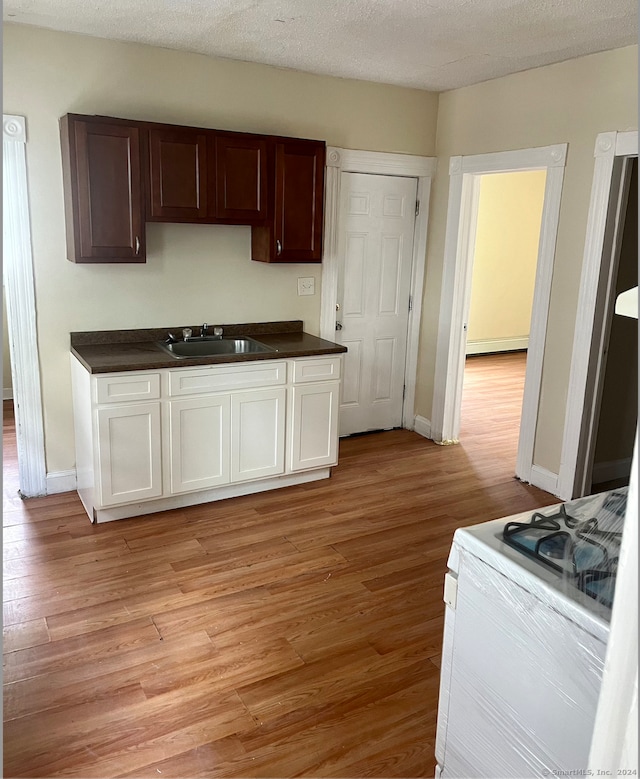 kitchen with a textured ceiling, sink, white range, and light wood-type flooring