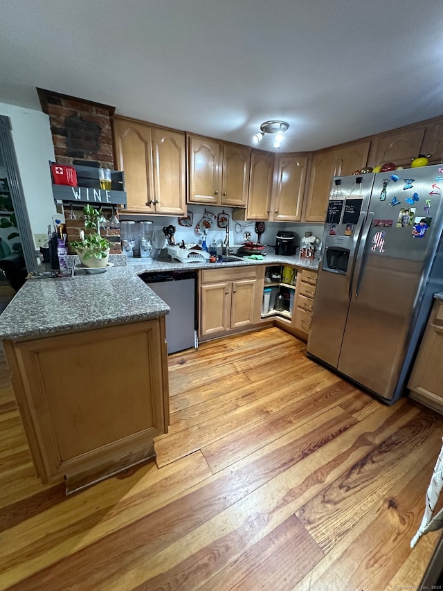 kitchen with light stone countertops, appliances with stainless steel finishes, kitchen peninsula, and light hardwood / wood-style flooring