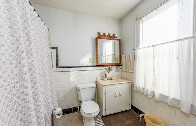 bathroom featuring a textured ceiling, vanity, toilet, and tile walls