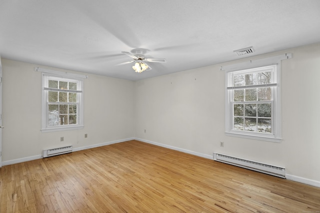 empty room with a wealth of natural light, light wood-type flooring, and a baseboard heating unit