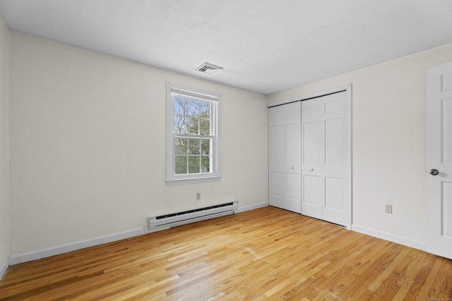 unfurnished bedroom with a closet, light hardwood / wood-style floors, and a baseboard heating unit