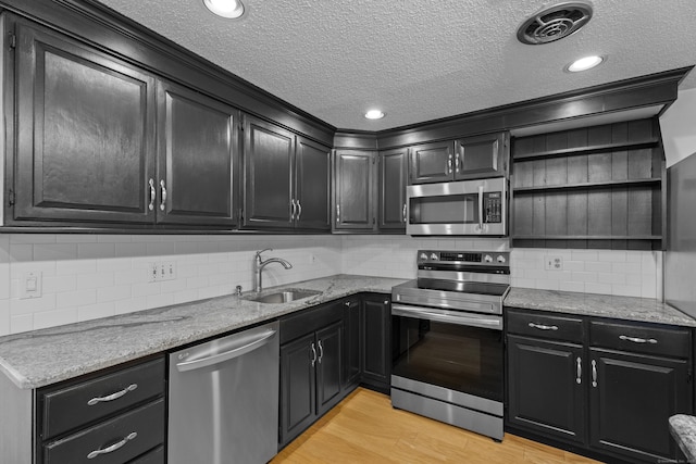 kitchen featuring appliances with stainless steel finishes, backsplash, light stone counters, sink, and light hardwood / wood-style floors