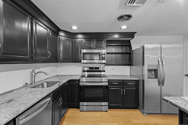 kitchen with light wood-type flooring, tasteful backsplash, light stone counters, stainless steel appliances, and sink