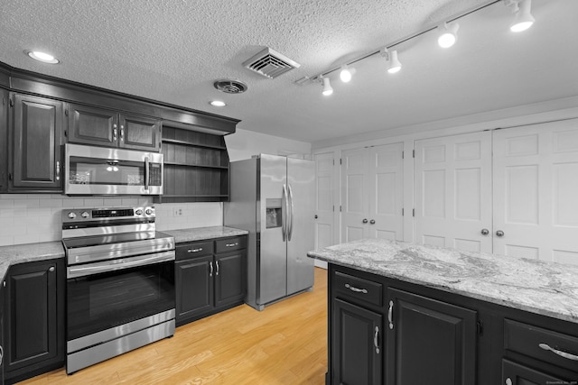 kitchen with light stone countertops, appliances with stainless steel finishes, tasteful backsplash, a textured ceiling, and light hardwood / wood-style flooring