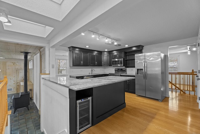 kitchen featuring light wood-type flooring, a textured ceiling, light stone countertops, stainless steel appliances, and beverage cooler