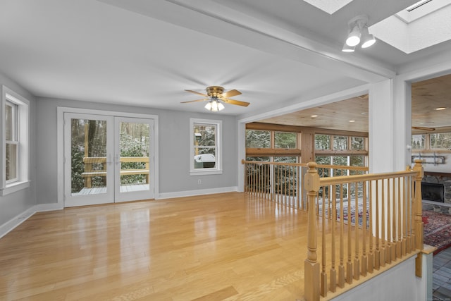 living room featuring a skylight, a stone fireplace, ceiling fan, and light hardwood / wood-style flooring