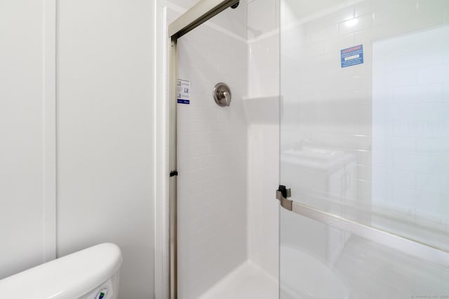 bathroom featuring a shower with door and toilet