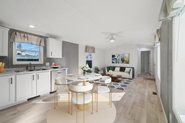 kitchen with vaulted ceiling, sink, dishwasher, white cabinets, and light hardwood / wood-style floors