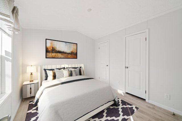 bedroom with light wood-type flooring, lofted ceiling, ornamental molding, and multiple windows