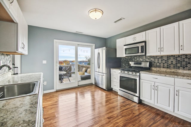 kitchen featuring appliances with stainless steel finishes, dark wood-type flooring, sink, dark stone countertops, and white cabinetry