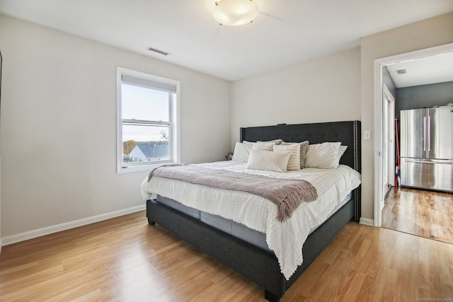 bedroom featuring light wood-type flooring and stainless steel refrigerator