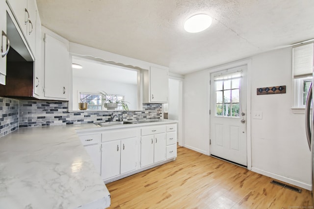 kitchen with white cabinetry, sink, backsplash, a textured ceiling, and light wood-type flooring