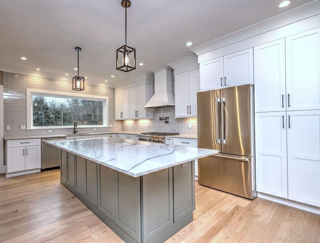 kitchen featuring pendant lighting, a center island, light stone countertops, appliances with stainless steel finishes, and custom range hood