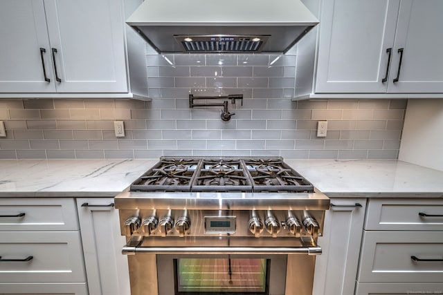 kitchen with high end range, backsplash, light stone countertops, and wall chimney exhaust hood