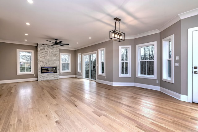 unfurnished living room featuring a stone fireplace, light hardwood / wood-style floors, ceiling fan with notable chandelier, and ornamental molding