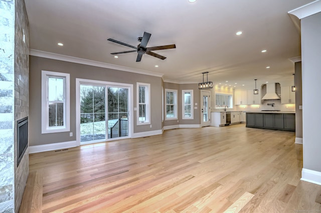 unfurnished living room with sink, light hardwood / wood-style floors, a fireplace, ceiling fan with notable chandelier, and ornamental molding