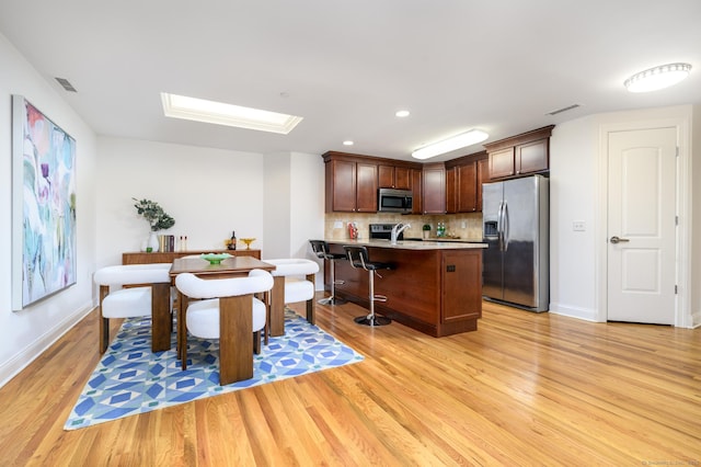 kitchen with light hardwood / wood-style flooring, a breakfast bar, appliances with stainless steel finishes, a skylight, and tasteful backsplash