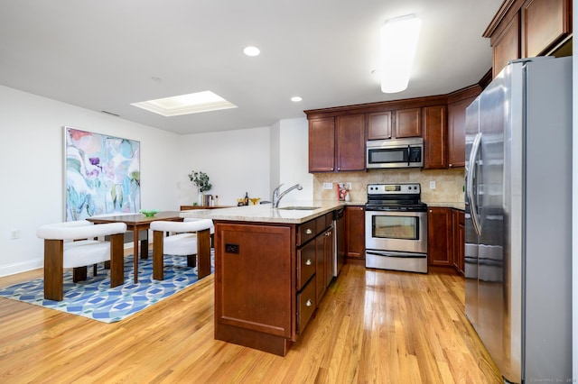 kitchen with sink, a skylight, light wood-type flooring, stainless steel appliances, and decorative backsplash